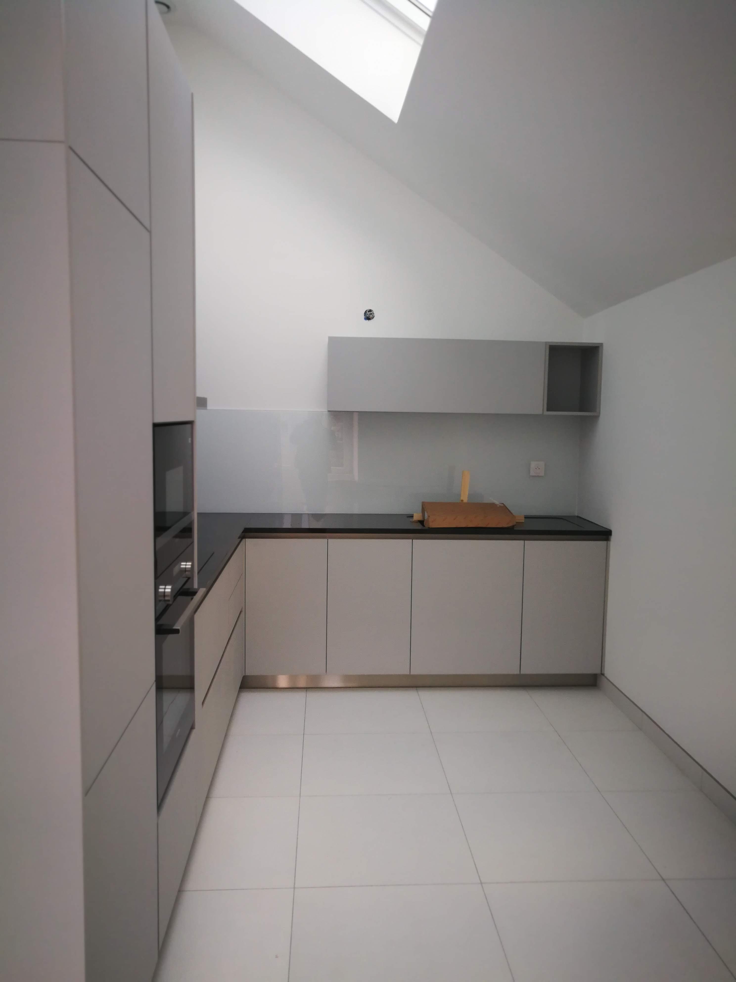 Cozinha em mansarda com armarios cinza claro, bancada preta e claraboia no teto inclinado