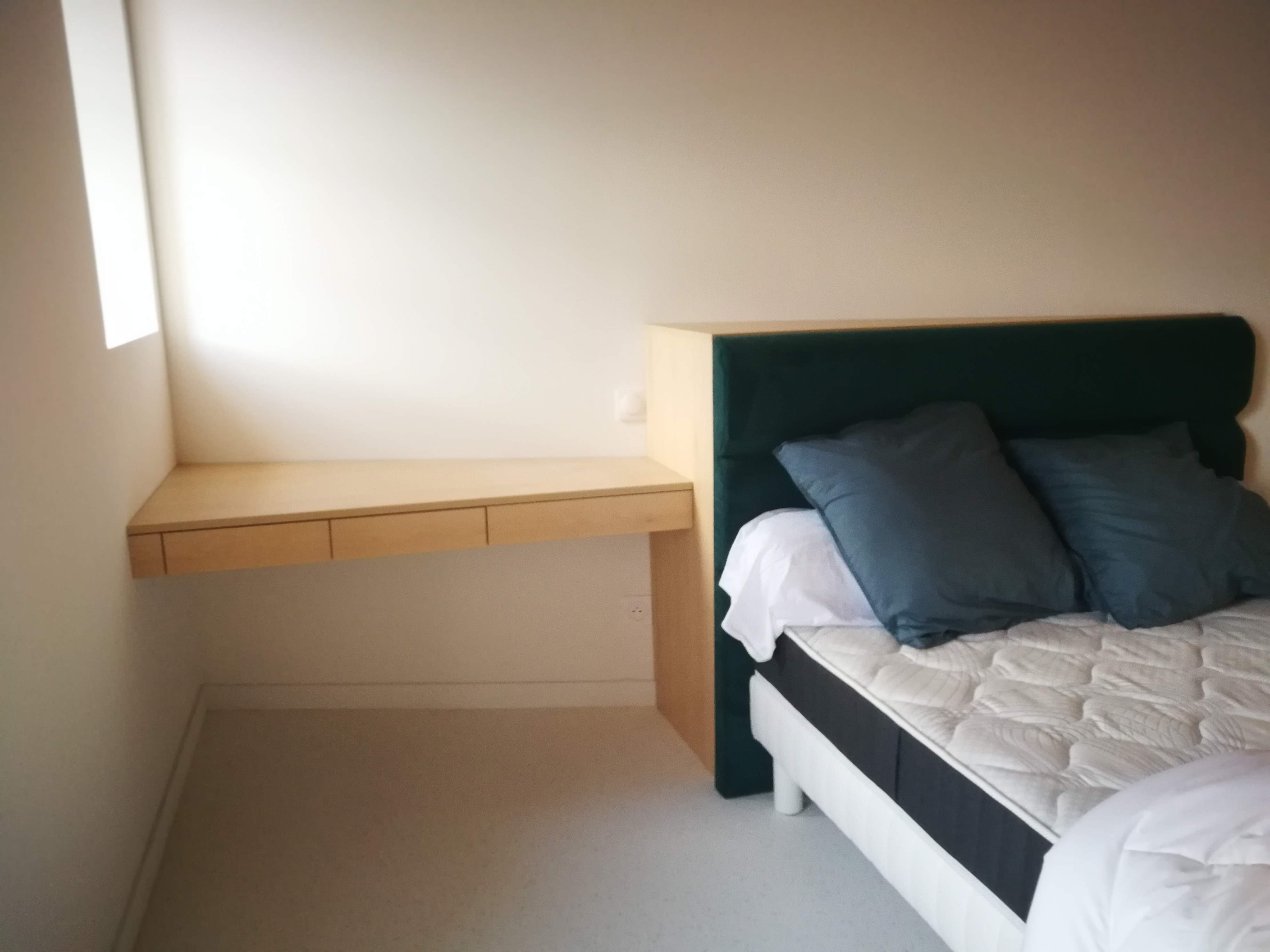 Quarto com cabeceira estofada em veludo verde-escuro e mesa de cabeceira suspensa em madeira clara